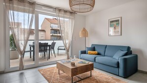A modern living room with a blue sofa, a wooden coffee table, and a large window with curtains. - Apartment for 4, center and seaside (Saint-Brevin-les-Pins)