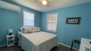 A bedroom with a bed, two windows, a ceiling fan, a nightstand, and a dresser.