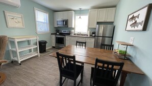 A compact kitchen with white cabinets, a stainless steel refrigerator, a microwave, and a dining table with chairs.