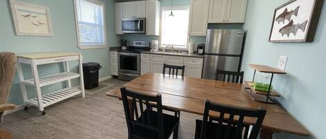 A compact kitchen with white cabinets, a stainless steel refrigerator, a microwave, and a dining table with chairs.