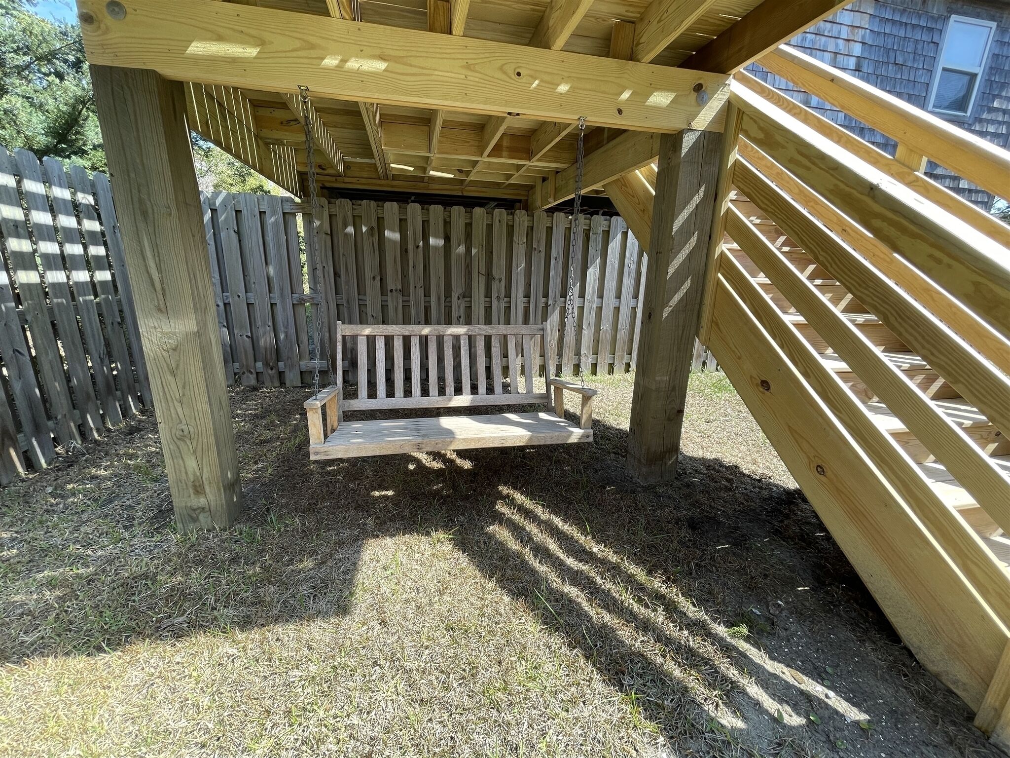A wooden swing set under a wooden structure with a metal chain.