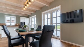 A modern kitchen with a dining area, large windows, and a flat-screen TV. - Doppelhaushälfte in Karolinenkoog (Karolinenkoog)