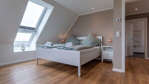 A bedroom with a sloped ceiling, a bed, a nightstand, and a window with a view. - Doppelhaushälfte in Karolinenkoog (Karolinenkoog)