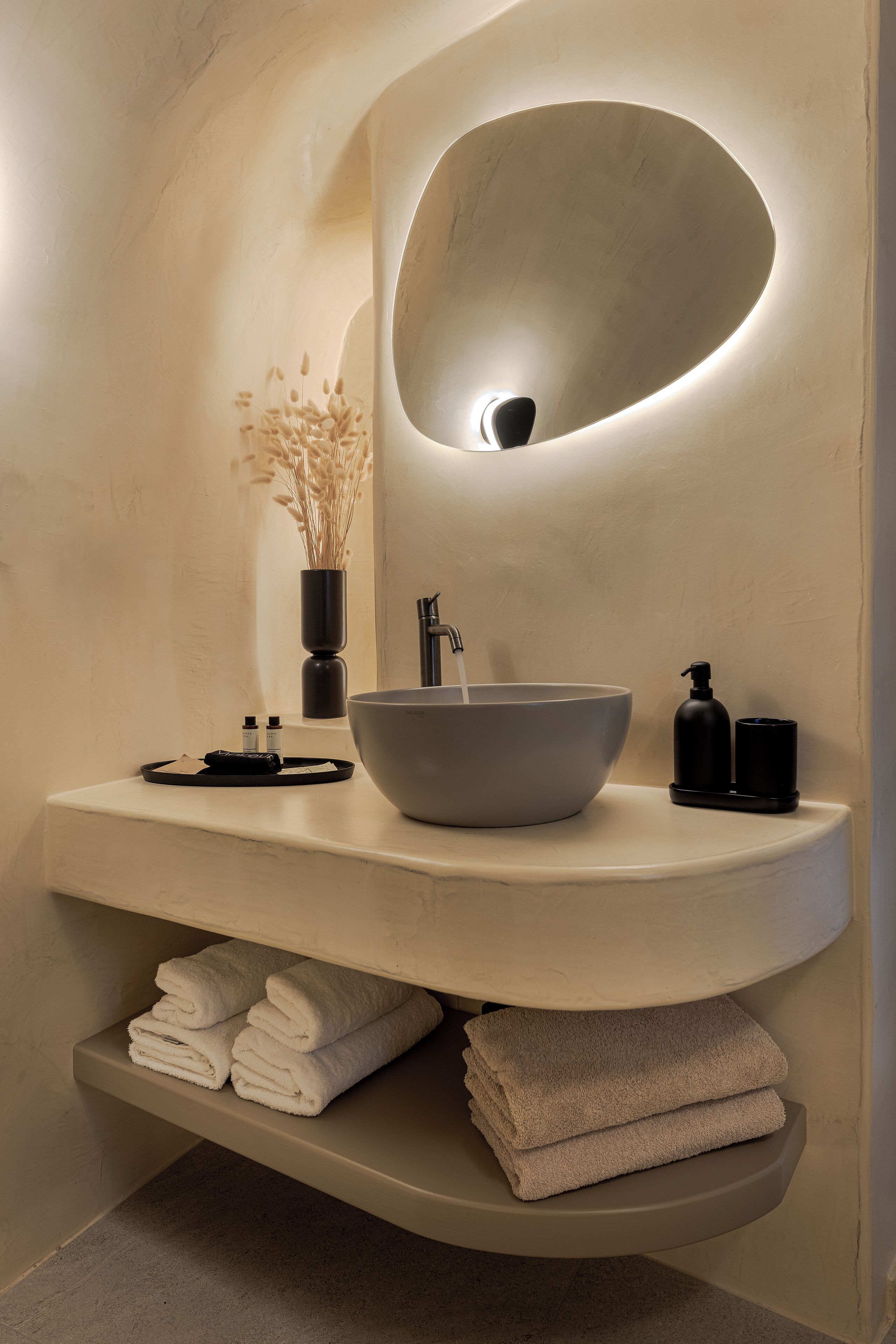 A modern bathroom with a large oval sink, a mirror, and a shelf with folded towels.