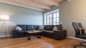 Uma sala de estar moderna com um sofá seccional cinza escuro, uma mesa de centro de madeira e um abajur.