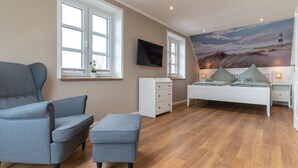 Quarto com uma cama, uma cadeira, uma mesinha, uma televisão e uma janela.