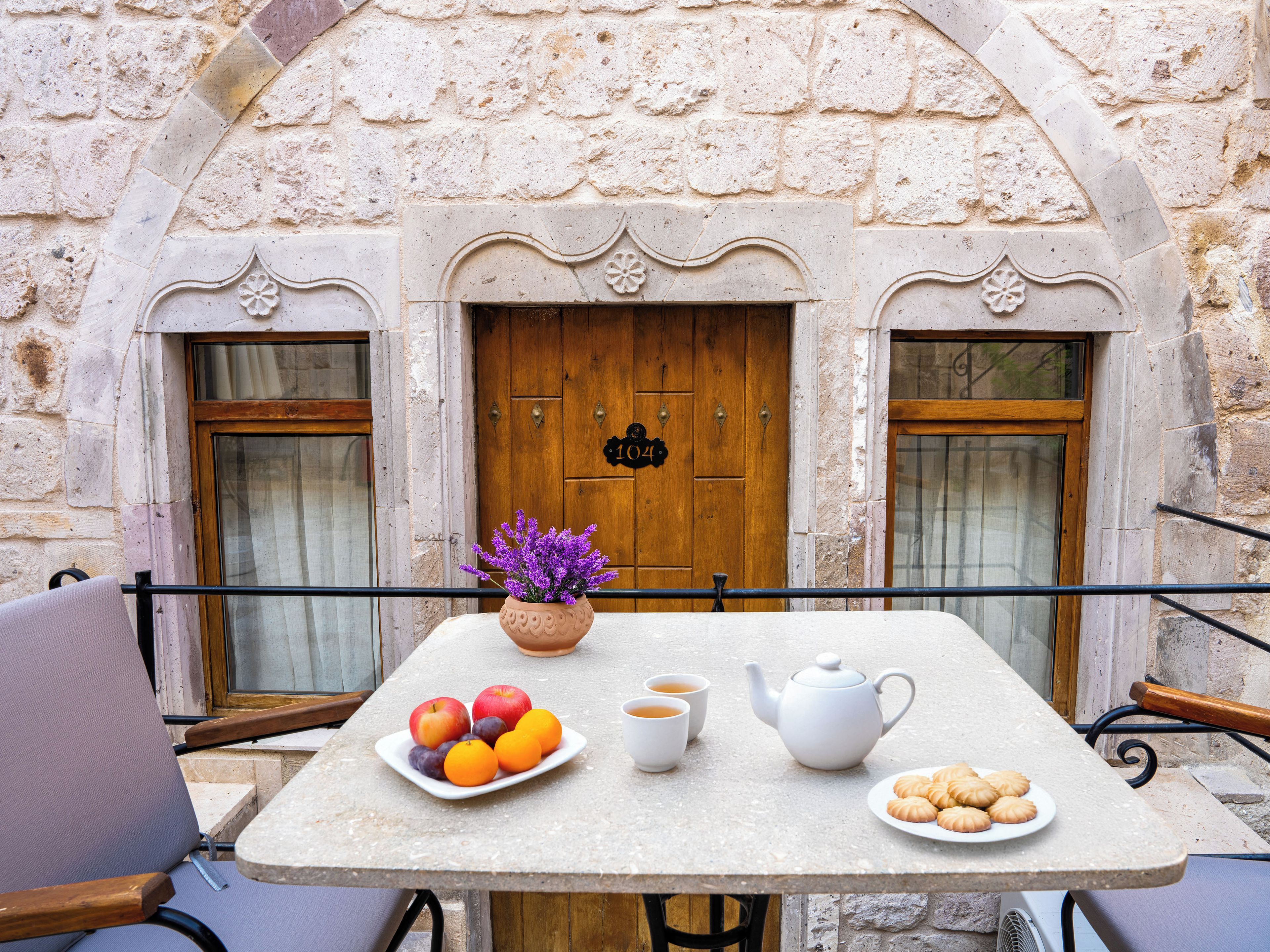 A table set with fruits, tea, and cookies outside a building with a stone facade and wooden doors.