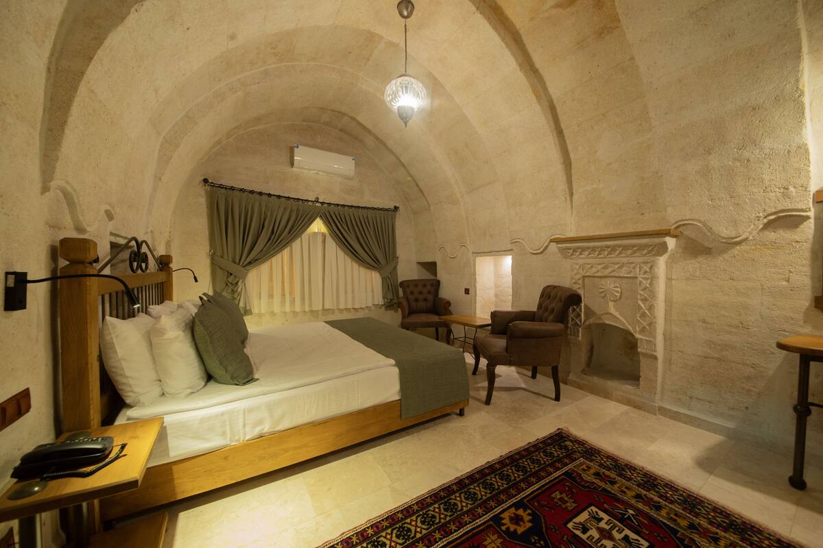 A room with a bed, two armchairs, a small table, a fireplace, and a patterned rug.