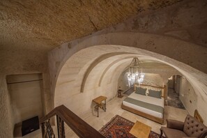 A spacious room with a large bed, a wooden table, and a chandelier. - Ares Cave Suites (Nevsehir)