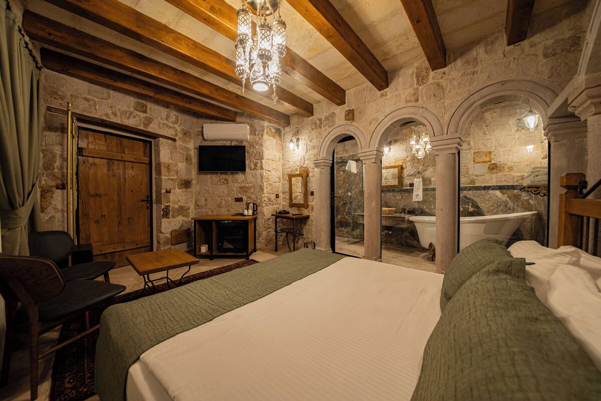 A rustic room with a large bed, wooden furniture, stone walls, and a stone fireplace.