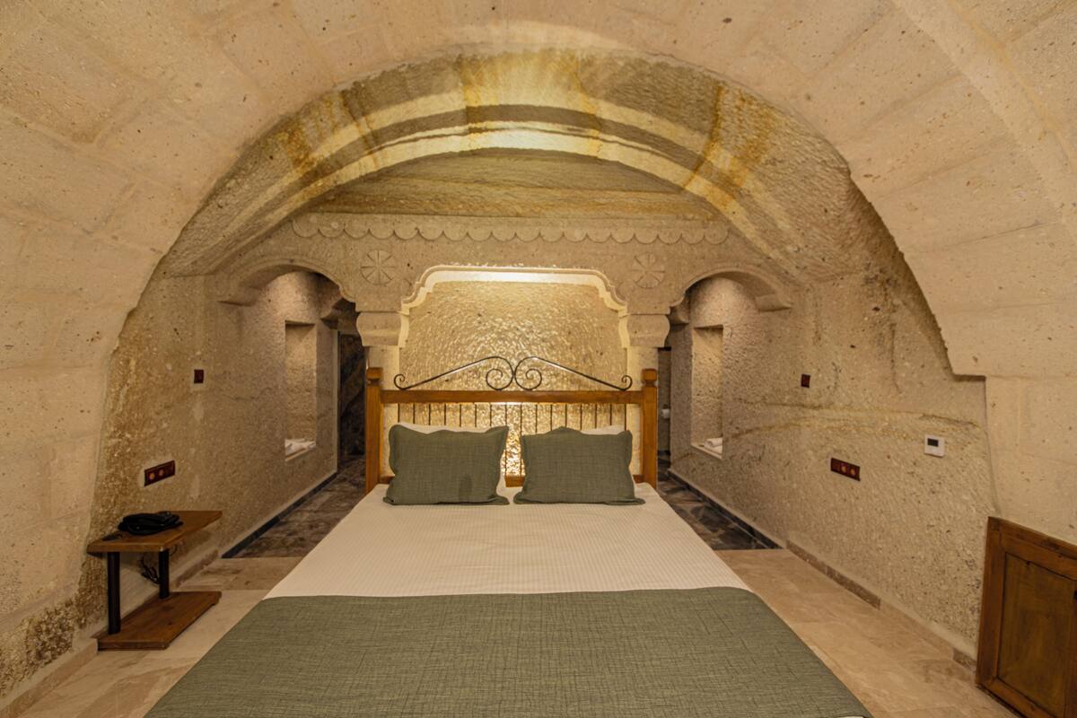 A room with a large bed, a wooden headboard, and a stone archway.