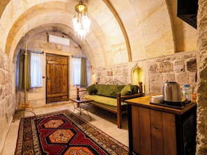 Una habitación acogedora con pared de piedra, puerta de madera, un banco, una mesa con hervidor y un tapete estampado.