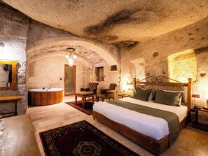 A rustic bedroom with a stone wall, a wooden bed, a round sink, and a wooden bench. - Ares Cave Suites (Nevsehir)
