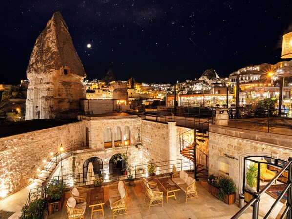 Terraço no telhado com paredes de pedra, área de estar ao ar livre e vista da cidade à noite.