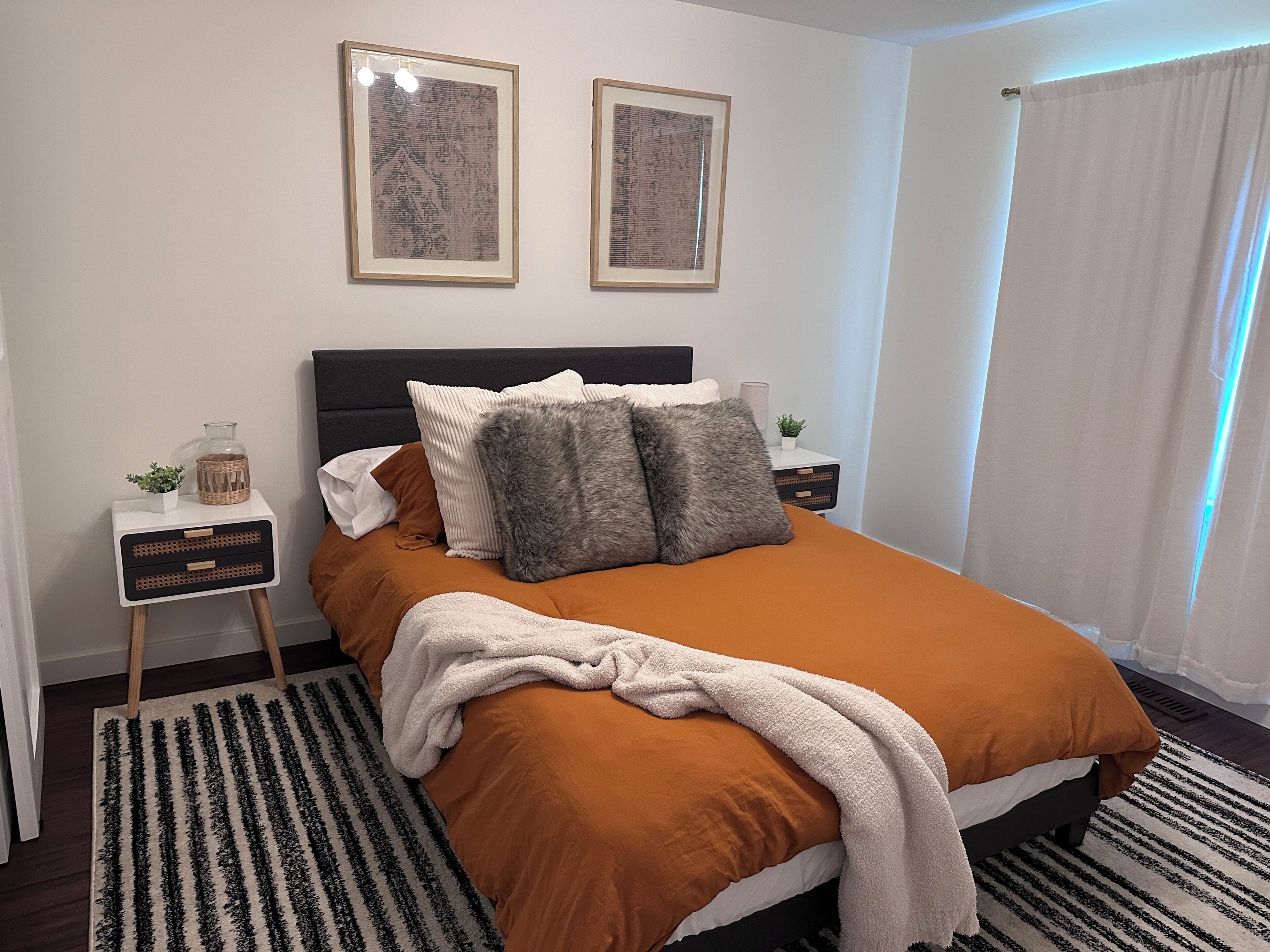 Un dormitorio ordenado con una cama, mesitas de noche y dos cuadros en la pared.