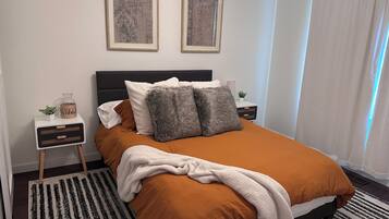 Un dormitorio ordenado con una cama, mesitas de noche y dos cuadros en la pared.