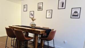 Un coin repas avec une table en bois, quatre chaises marron et un vase contenant des plantes séchées.