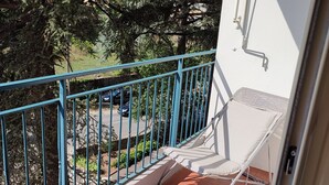 A balcony with a red-tiled floor, a white chair, and a blue railing. - Studio Pour Cures Thermales Entièrement Refait et Équipé Pour 2 Personnes (Gréoux-les-Bains)