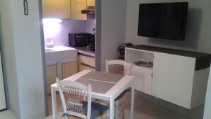 A compact kitchen with a dining table, chairs, a microwave, a stove, and a TV mounted on the wall. - Studio Pour Cures Thermales Entièrement Refait et Équipé Pour 2 Personnes (Gréoux-les-Bains)