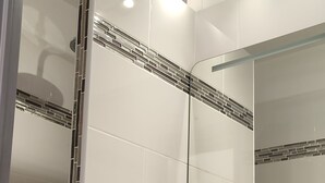 A bathroom with white tiles, a mirror, a sink with a soap dispenser, and a towel rack. - Studio Pour Cures Thermales Entièrement Refait et Équipé Pour 2 Personnes (Gréoux-les-Bains)