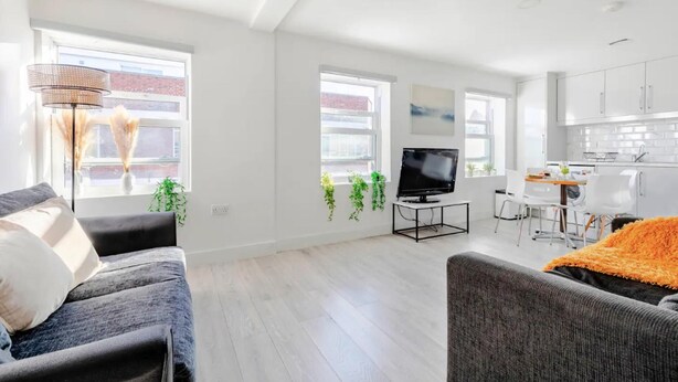 A modern apartment with a living room, dining area, and kitchen. There are large windows, a flat-screen TV, and a dining table with chairs. - 1-bed in Bricklane / Shoreditch - 6 Sleeps (London)