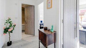 A hallway with a wooden door, a small table with a green statue, and a potted plant with pink flowers. - 1-bed in Bricklane / Shoreditch - 6 Sleeps (London)
