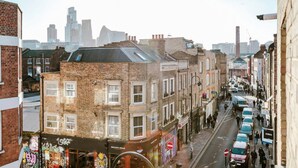 A street view with a row of brick buildings, some shops, and parked cars. - 1-bed in Bricklane / Shoreditch - 6 Sleeps (London)