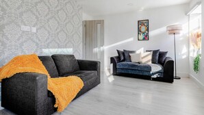 A modern living room with two sofas, one with an orange throw, and a floor lamp. - 1-bed in Bricklane / Shoreditch - 6 Sleeps (London)