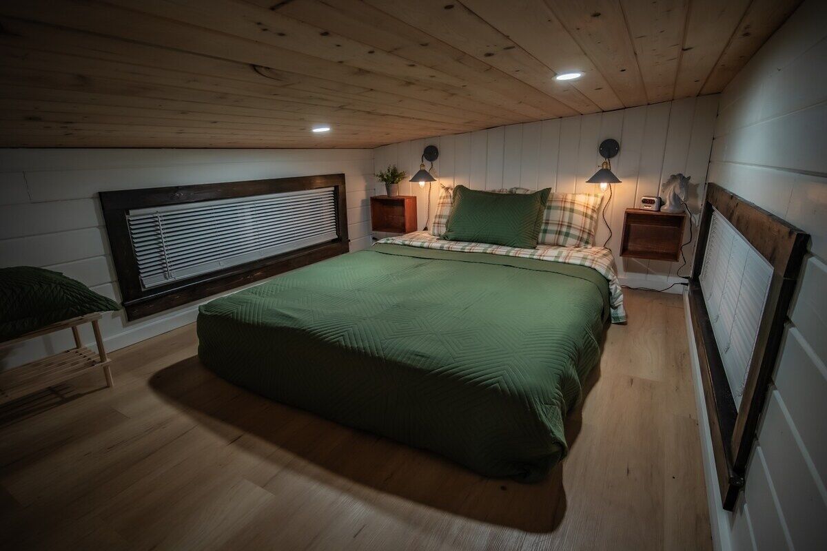 A bedroom with a large bed, wooden ceiling, and a window with blinds.