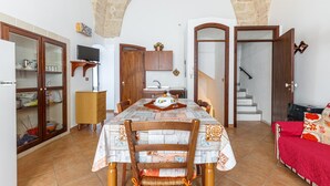 Ein Essbereich mit einem Tisch für vier Personen, einem Holzschrank mit Glastüren, einem Fernseher auf einem Lowboard und einer Treppe, die in einen anderen Raum führt.