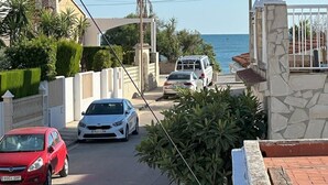 A coastal street with parked cars, a clear sky, and a view of the sea.