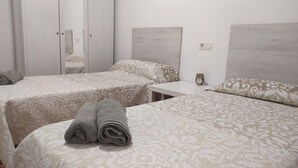A hotel room with two beds, a small table, a mirror, and a clock.