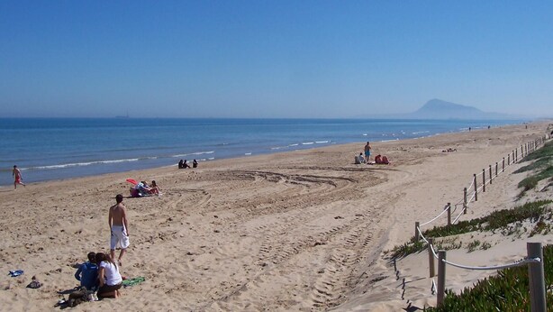 A beach with people sunbathing and walking along the shore.