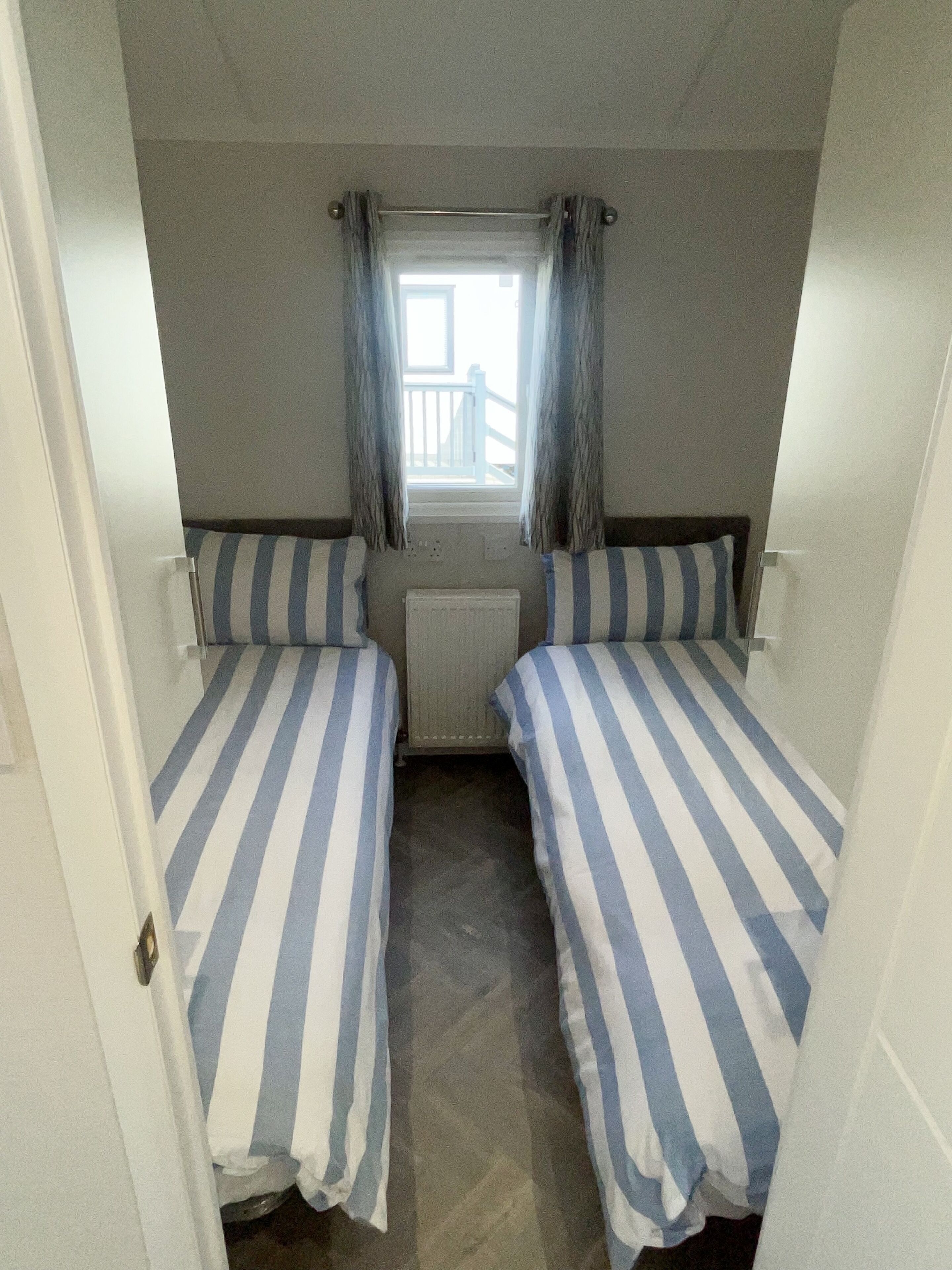 Ein kleiner, schmales Zimmer mit zwei Einzelbetten, einem Fenster mit Vorhängen und einer Heizung.