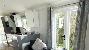 A modern living room with a sofa, a coffee table, and a view of the kitchen and outside. - Modern Homely Chalet in Tuxford (Newark)