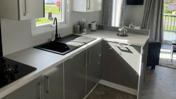 A modern kitchen with a built-in stove, a sink, and a dining area with a table and chairs. - Modern Homely Chalet in Tuxford (Newark)