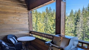 A wooden cabin with a patio featuring a grill, wicker chairs, and a table. - Grand Lodge 26 at the Official Collins Lake Resort (Government Camp)