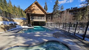 A pool area with a hot tub, surrounded by a wooden lodge and a fenced deck. - Grand Lodge 26 at the Official Collins Lake Resort (Government Camp)