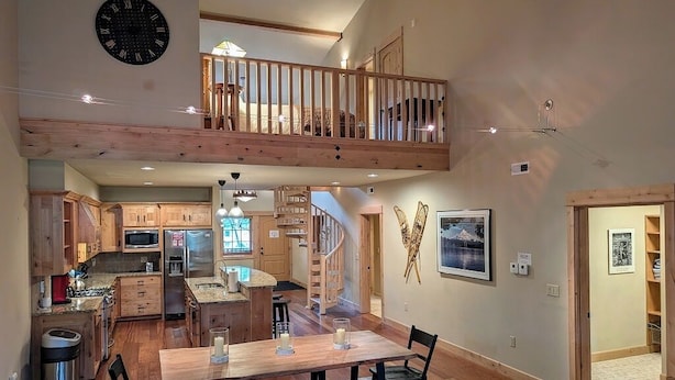 A spacious kitchen with wooden cabinets, a dining area with a large table, and a loft bedroom with a balcony. - Grand Lodge 26 at the Official Collins Lake Resort (Government Camp)