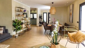 Een ruime woonkamer met een eettafel, stoelen en een bank. Er staat een boekenkast vol boeken en decoratieve objecten.