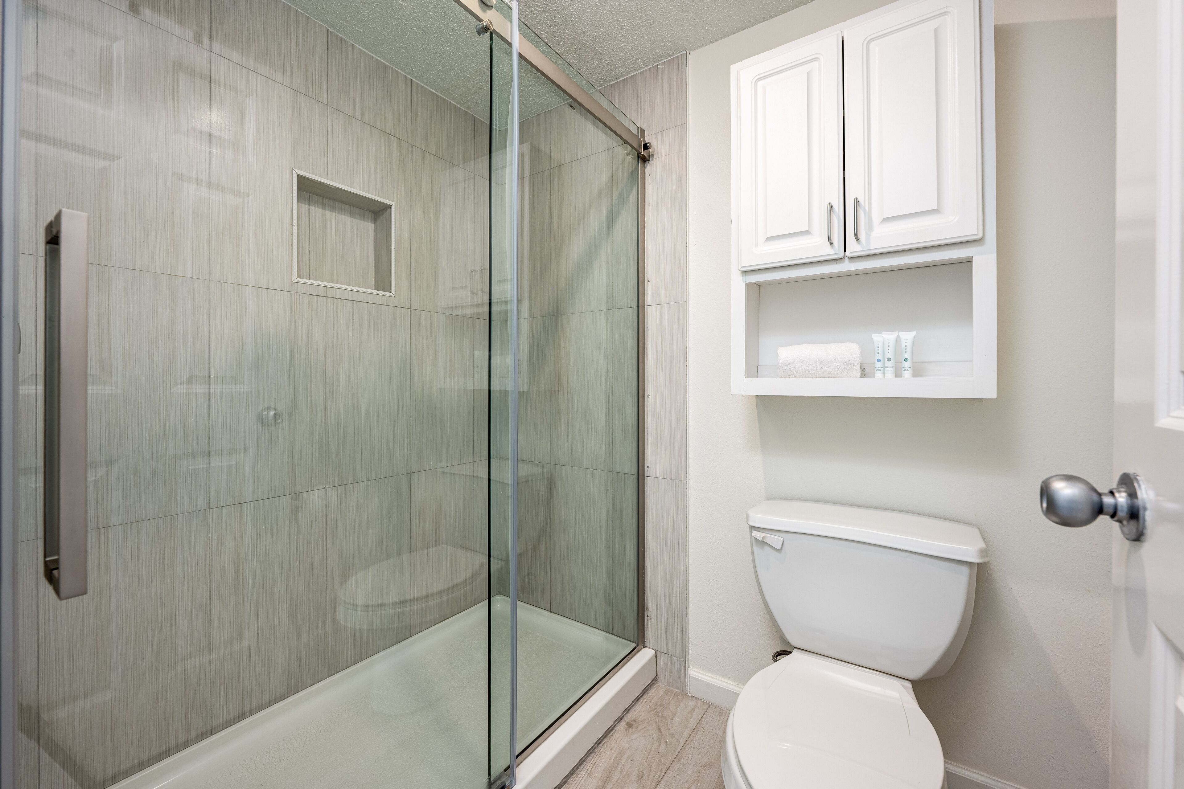Een badkamer met een douche met glazen wand, een toilet en een kastje met toiletartikelen.