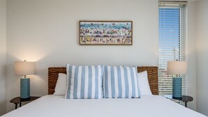 A neatly made bed with striped pillows, two bedside lamps, and a beach-themed painting on the wall. - Terrace @ Pelican Beach Resort 307b * Hotel accommodation * Salt Water Vacations (Destin)