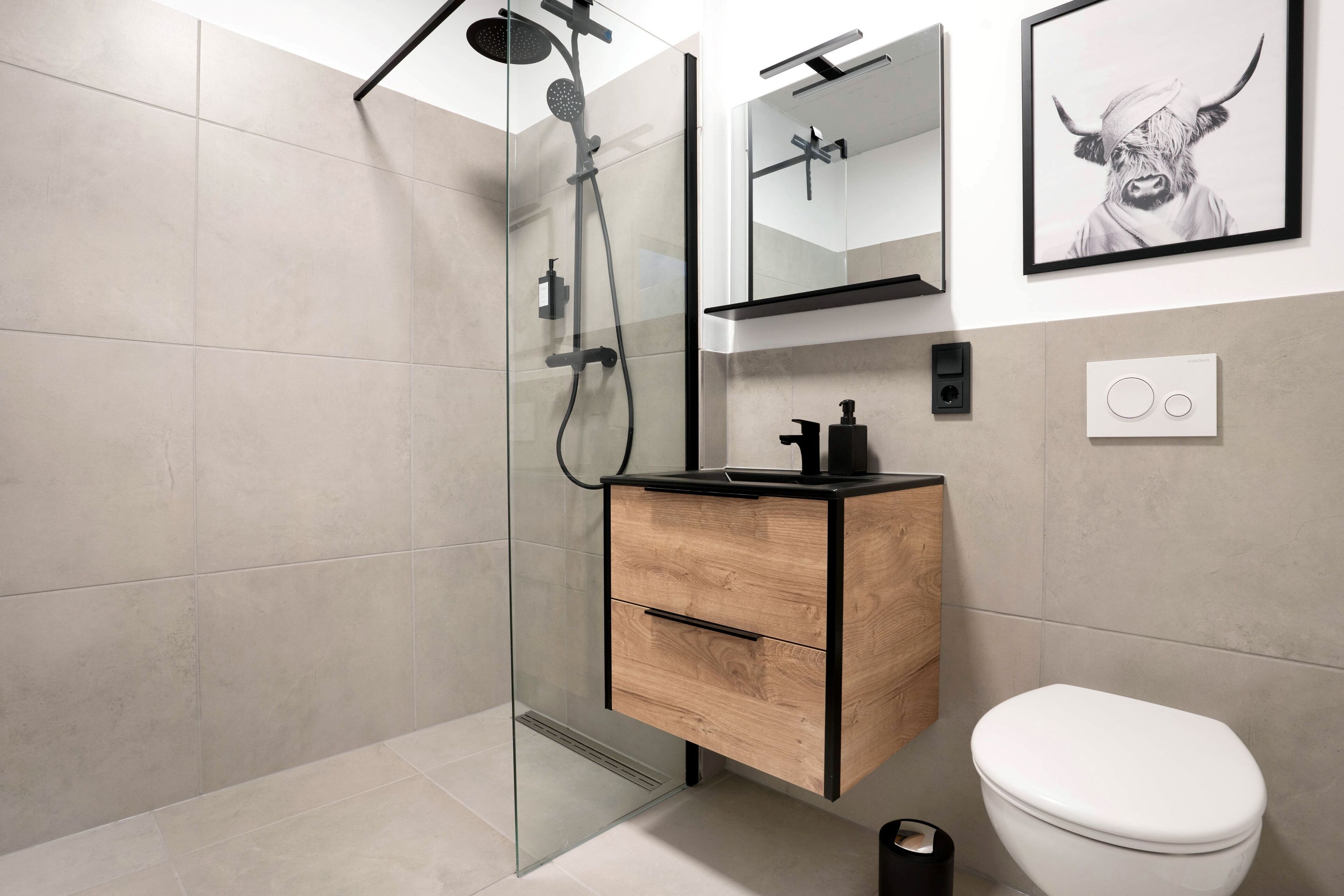 Un baño moderno con ducha envuelta en vidrio, tocador de madera, inodoro blanco y una obra de arte enmarcada en la pared.