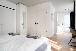 A modern hotel room with a large bed, two doors, a chair, and a view of the hallway. - Schicke Apartments in Bonn I home2share (Bonn)