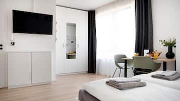 Una habitación de hotel moderna con una cama grande, un escritorio con silla, un televisor montado en la pared y una pequeña área de kitchenette.