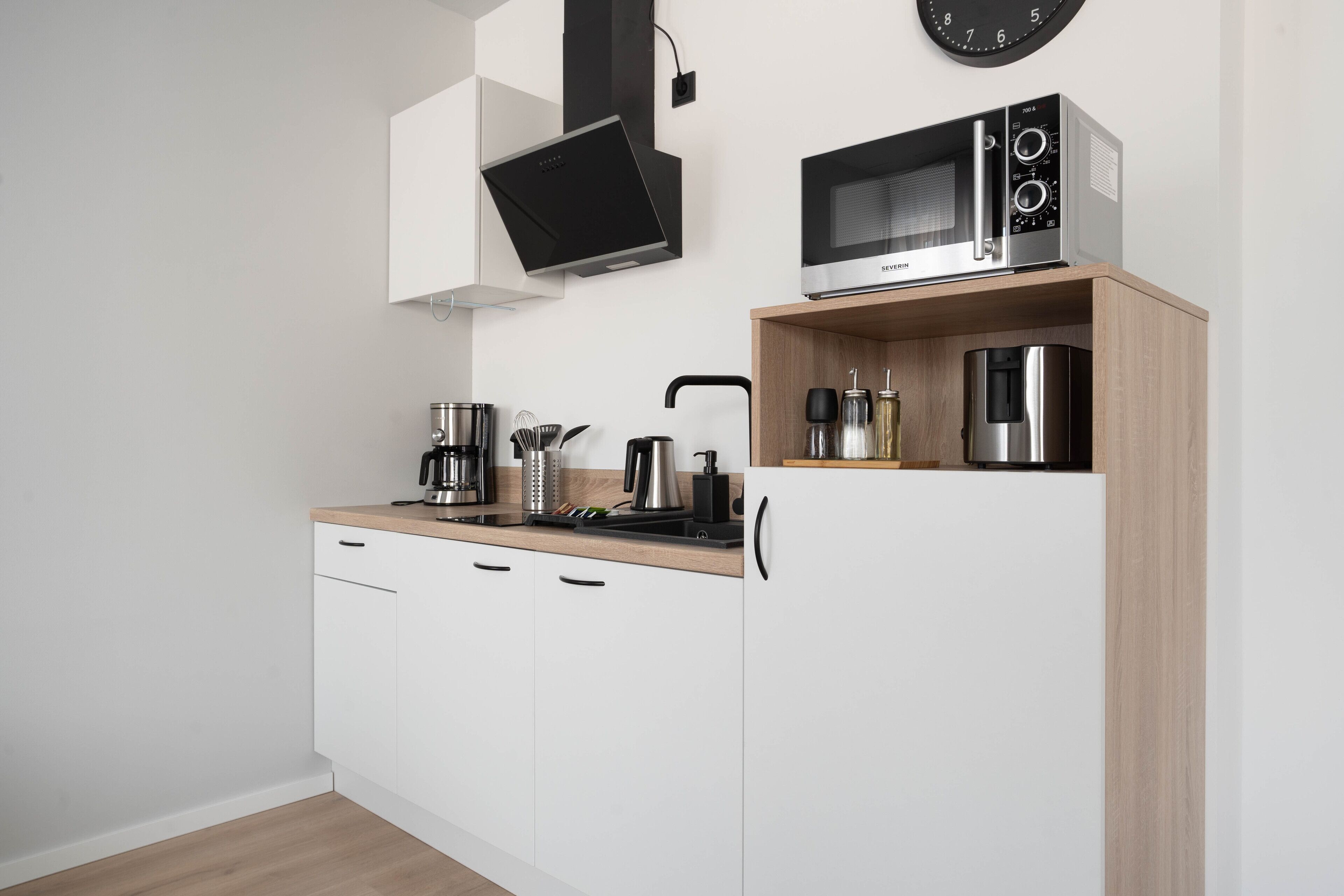 A modern kitchen with white cabinets, a wooden countertop, a built-in microwave, and a coffee maker.