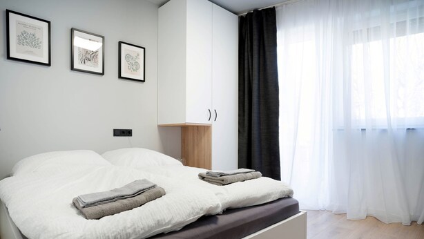 A modern bedroom with a large bed, a bedside table, and a wardrobe. - Schicke Apartments in Bonn I home2share (Bonn)