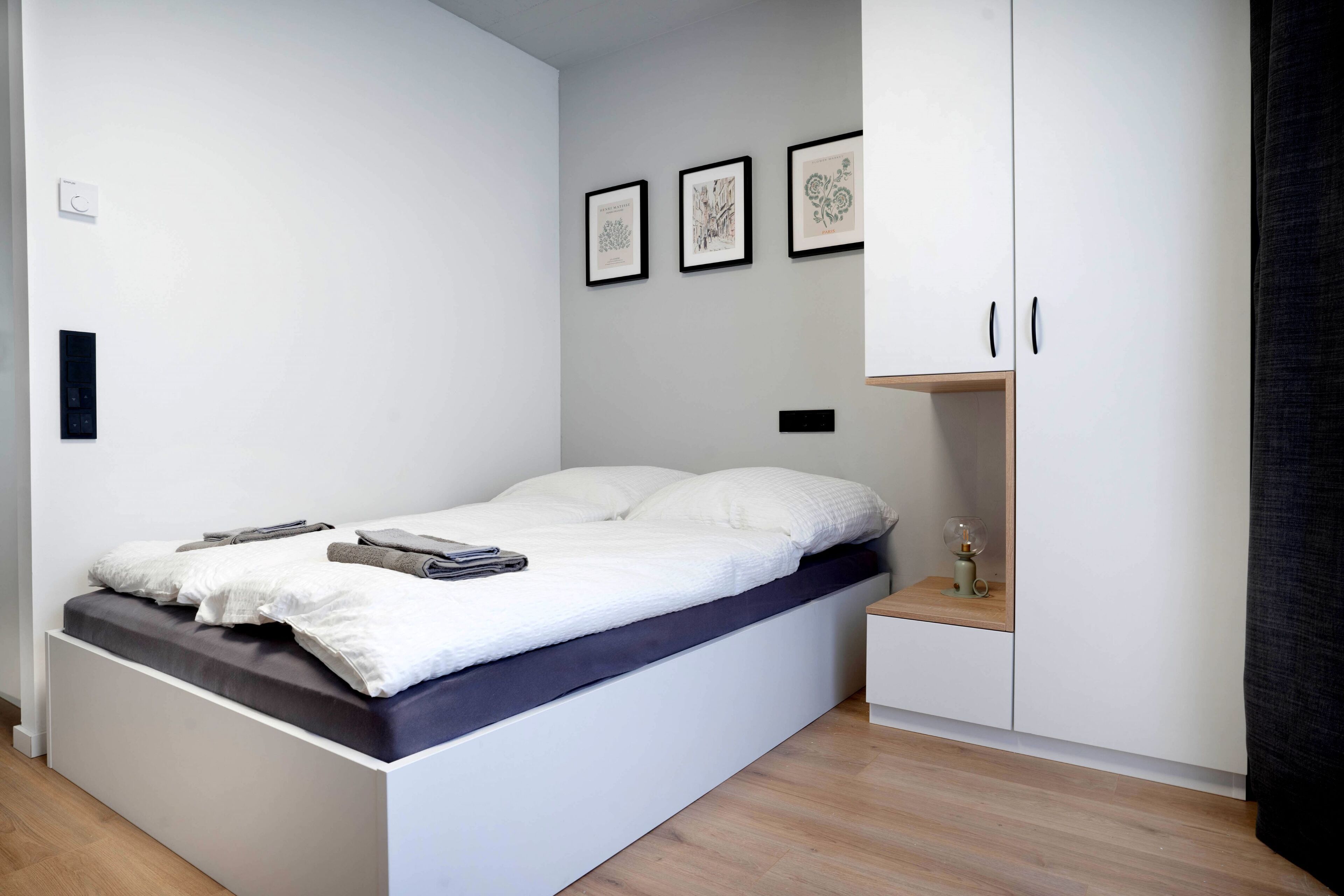 Un dormitorio moderno con cama, mesita de noche, armario y tres cuadros en la pared.