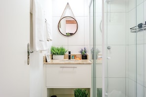 A bathroom with a white vanity, a round mirror, and a glass shower enclosure. - Apartamento Próximo ao Allianz Parque (São Paulo)