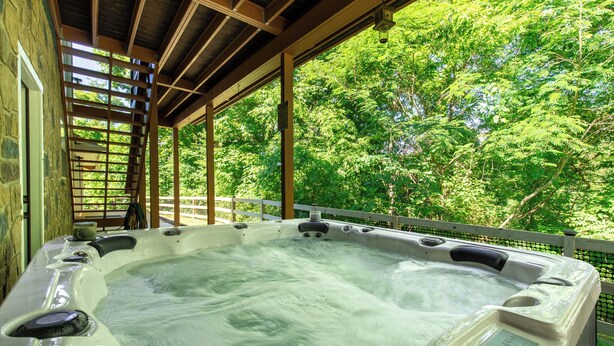A hot tub in a covered outdoor area with a wooden ceiling and stone walls, surrounded by lush greenery. - Lakeside Paradise Escape/Jet Ski & Kayak Adventure (Dandridge)